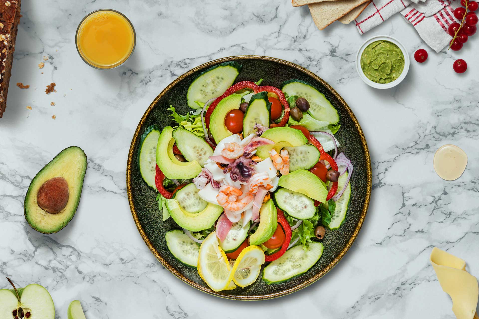 Una ciotola di insalata con gamberi, avocado, pomodori e pane.